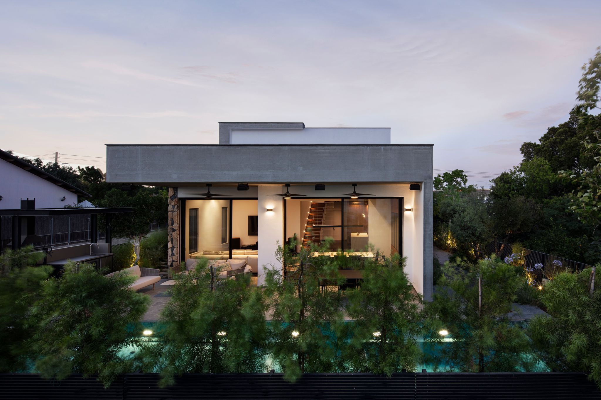The villa at dusk in Poria Illit, its glazed façade lit up and the pool in the foreground