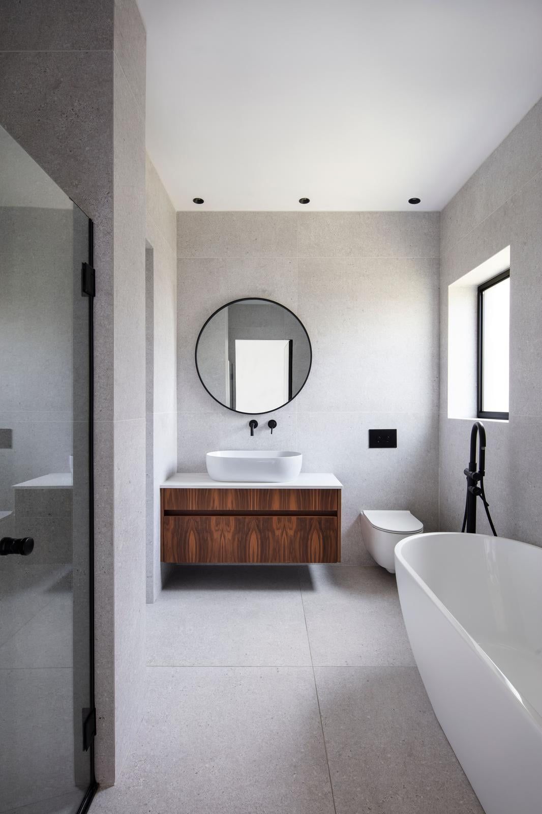 Bathroom with freestanding bathtub, wooden vanity and round mirror